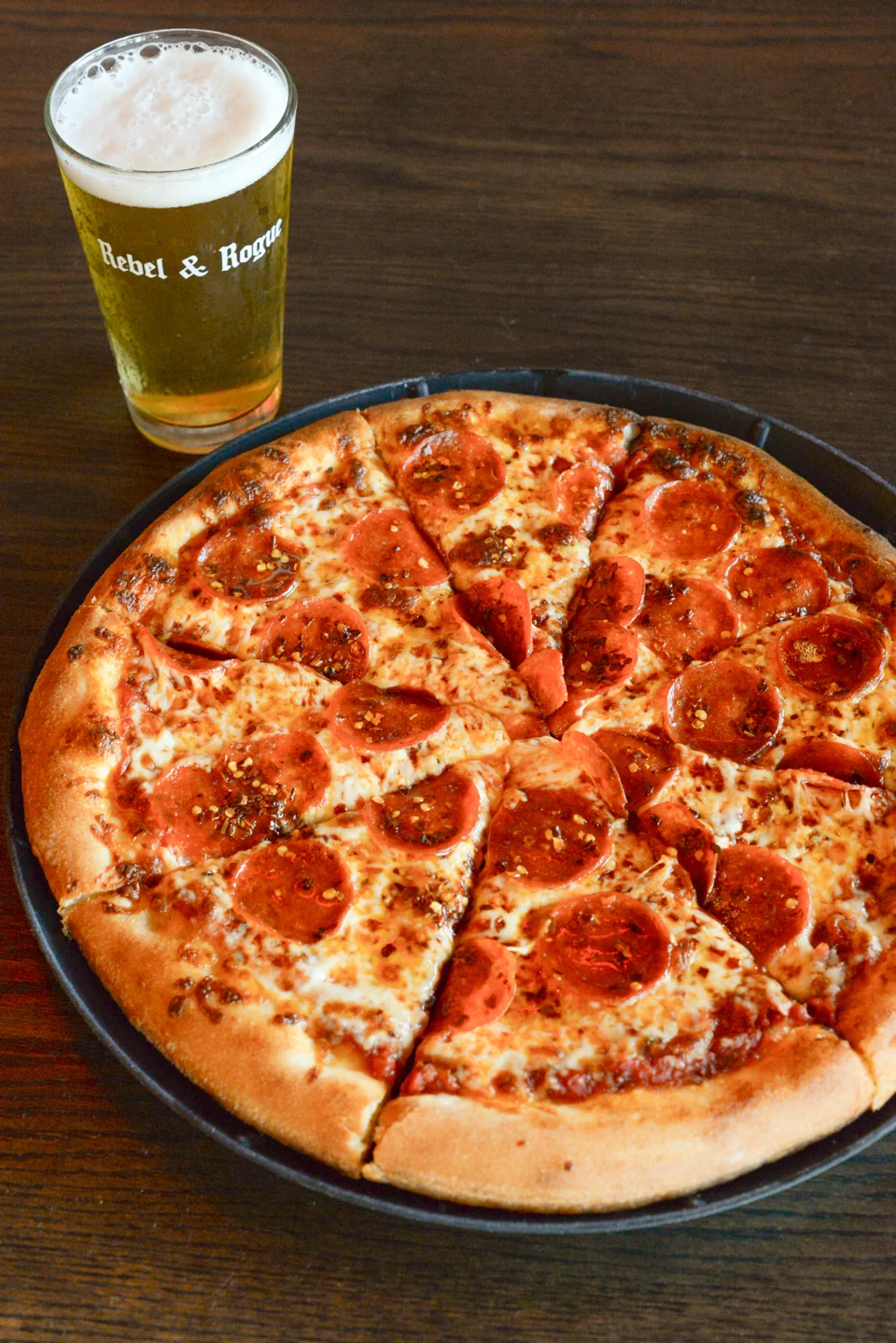 Rebel & Rogue pepperoni pizza beside a branded pint glass. Beer sold separately.